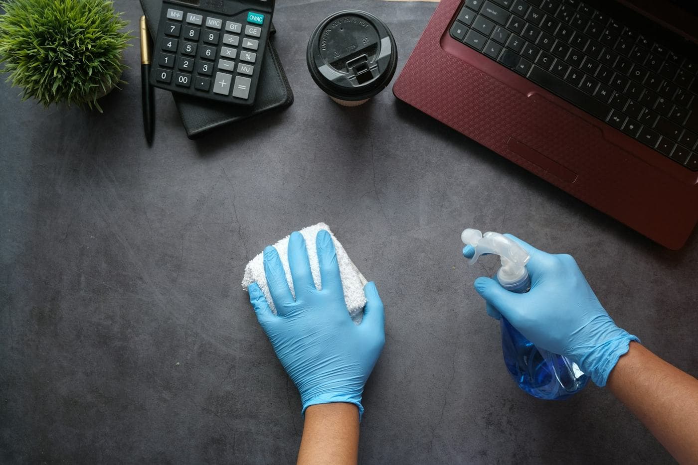 Gloved hands disinfecting a desk
